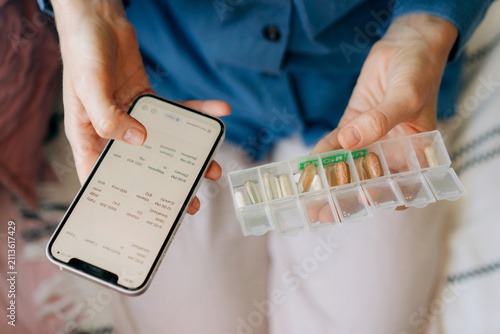 Close-up cropped view of a vitamin pill organizer and mobile phone in the hands of a woman.