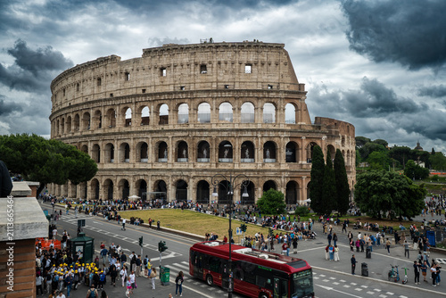 Obraz na płótnie The historic Roman Colosseum surrounded by tourists and a red bus on a cloudy day