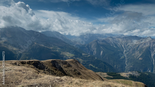 Breathtaking high-altitude landscape in the Valais region of Switzerland, featuring a dramatic, steep green mountain ridge. 