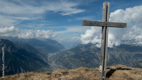 A majestic, weathered wooden summit cross stands prominently on a grassy mountain peak  Folluhorn in the Swiss Alps