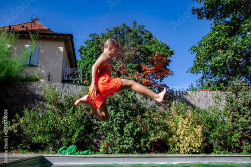 Foto Active boy jumps into a backyard swimming pool on a sunny summer day