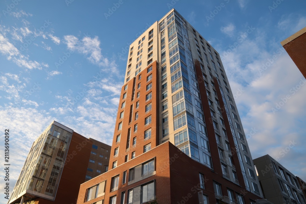 Fototapeta premium New Building facade with brown cladding. Modern apartment building in new development area. Bottom view. Blue sky. Paneling on modern architectural design urban setting. New modern building exterior