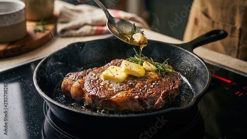 Chef basting a sizzling steak in a hot cast iron pan with butter and rosemary.