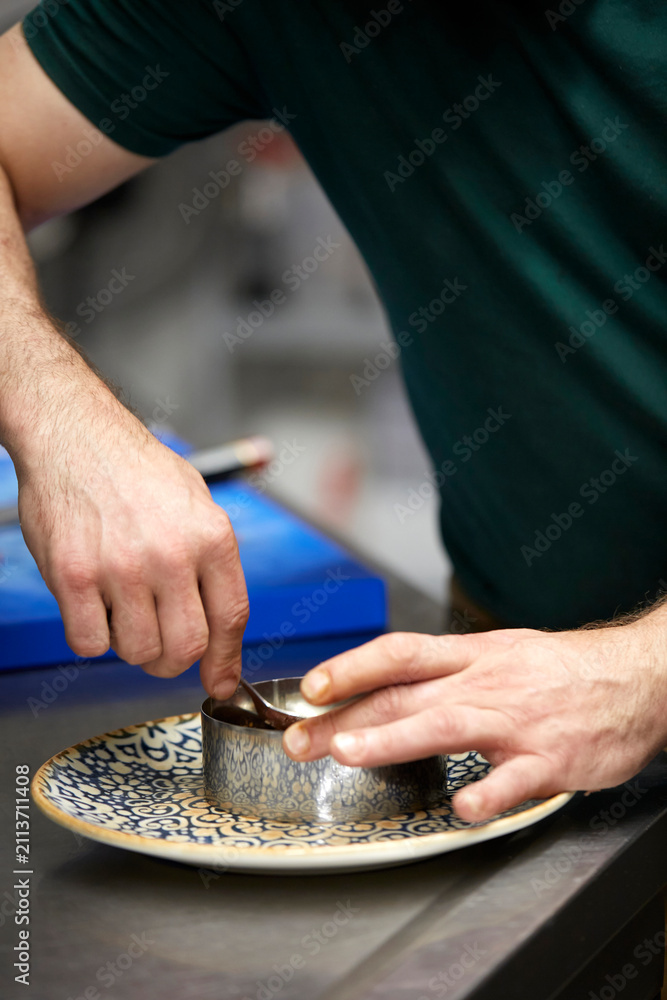 Fototapeta premium Close-up of chef hands shaping tartar in a ring mold with a spoon