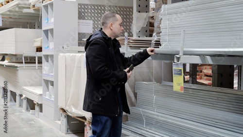 Fotografie Construction worker examining metal profiles, comparing specifications on smartp