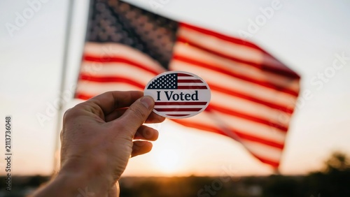 Person holding I Voted sticker with US flag background. American election.