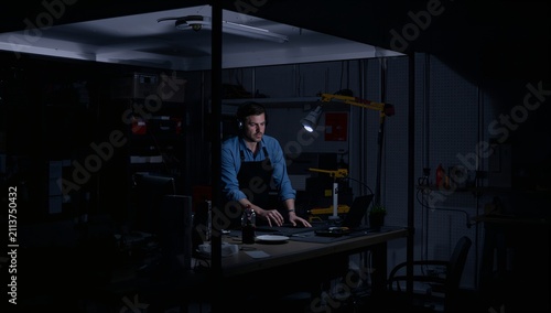 Man Working in a Dimly Lit Workshop at Night Focused on Tasks