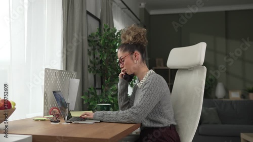 Young businesswoman multitasking in home office talking on the phone