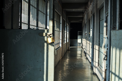 Canvas Print Dim prison hallway corridor with locked door brass padlock, iron bars shadow and