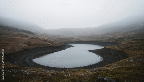 Foggy Landscape With a Round Lake in a Mountainous Area