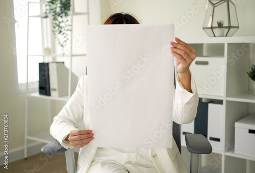 Blank poster mockup held by Asian businesswoman seated in modern office offering copy space for branding advertising recruitment corporate messaging and creative campaign presentation.