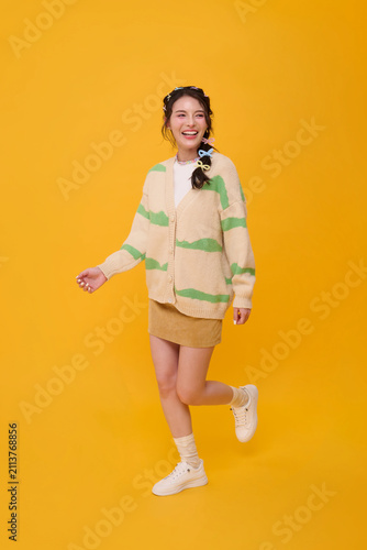 Asian woman smiling and posing on one leg in studio expressing youthful confidence cheerful lifestyle positive energy fashion appeal and playful individuality with copy space.