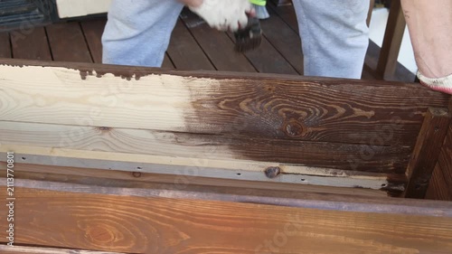 Brown oil for protection of wood by staining. Painting fence for protecting and pests. Woodworker applying finish to pine board box. Repairman varnishing with brush wooden fencing wall plank surface.