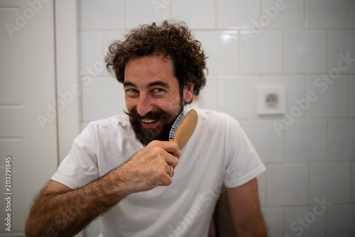 Happy man brushing beard in bathroom, self-care routine