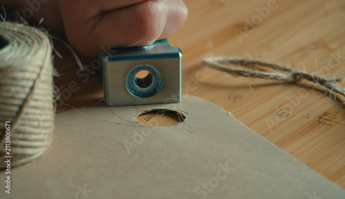 Close-up of a metal hole puncher piercing a cardboard tag on a table
​Categoria: Hobbies e Lazer