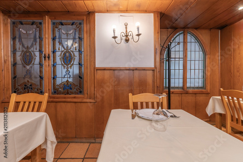 Cozy Wood-Paneled Dining Room with Stained Glass Windows, Brass Sconce, and Set Tables