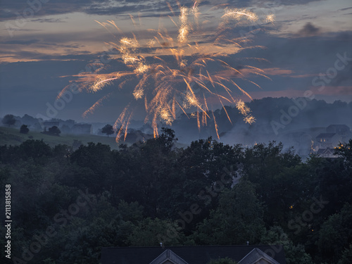 Cascading 4th of July fireworks trails falling over dark treetops in Pennsylvania with copyspace