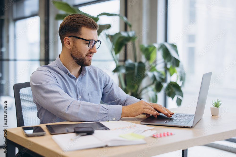 Fototapeta premium Young businessman working at desk, using laptop in modern office, focusing on productivity and technology