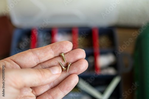 Obraz na plátne Close-up of a screw held between fingers before fastening wooden furniture with a power tool