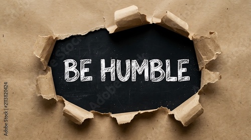 Be humble text written on a black background revealed through a torn brown paper hole