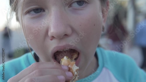 Hungry girl eating a burger outdoors, close-up of a child enjoying fast food