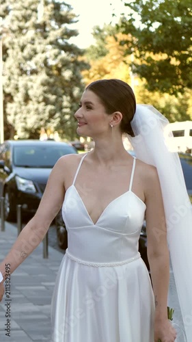 Happy newlywed couple kissing on city street while bride holding wedding bouquet.