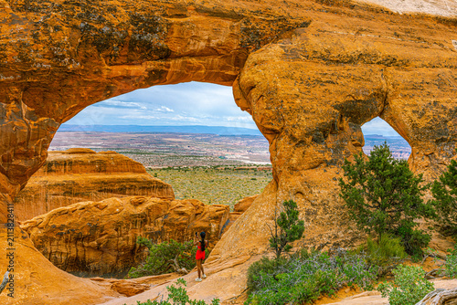 Foto A hiker in red stands beneath Partition Arch, framing a vast desert valley view in Devils Garden, Arches National Park