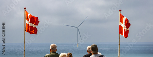 Danish flags and wind turbine by the sea, people watching