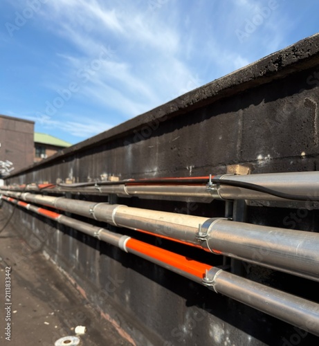Commercial rooftop electrical installation featuring galvanized metal conduits securely mounted along a parapet wall under a bright blue sky. The image showcases professional electrical infrastructure