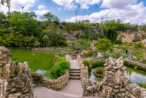 Fotografie High-angle shot looking down over stone bridges, walking paths, flowerbeds, and green ponds surrounded by limestone walls in San Antonio, Texas