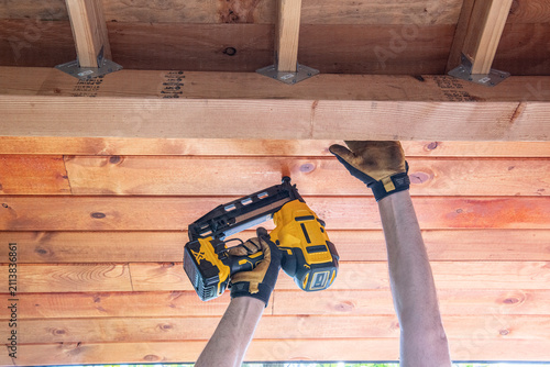 Obraz na plátně Close-up of a homeowner installing cedar roof boards using a cordless framing nailer during a backyard shed construction project