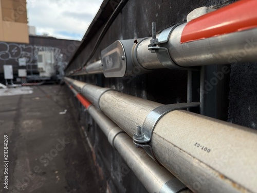 Close-up of a galvanized electrical conduit installation with a junction box mounted along a commercial rooftop parapet wall. The image showcases professional electrical infrastructure, conduit routin