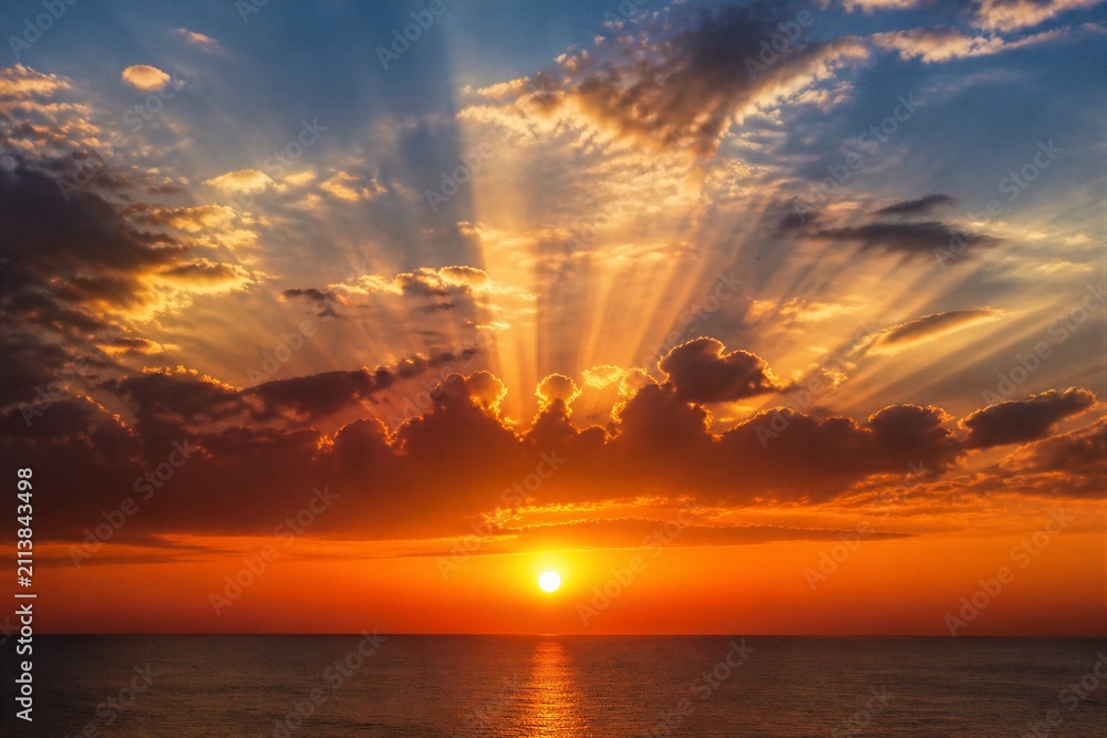 Fototapeta premium Sunrise sunbeams radiating over calm ocean horizon