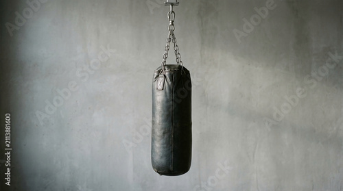 Black punching bag hanging against a concrete wall, symbolizing strength, training, and a classic gym aesthetic.