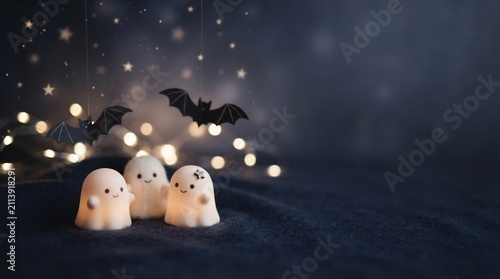 Cute glowing ghost figurines and hanging paper bats on a dark starry background for Halloween season design
