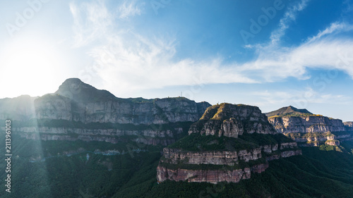 Quadro su tela Layered rocky mountain cliffs under a bright blue sky with sunlight illuminating the landscape