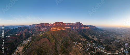 Konstfotografi Aerial wide panorama shows sunlit layered mountain ranges, surrounding valleys, rural settlements and clear sky at dawn