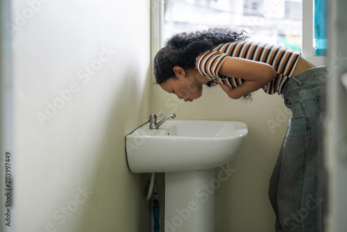 Sick young African American woman bending over a sink feeling nauseous and vomiting, representing stomach illness, food poisoning, morning sickness, and healthcare issues.