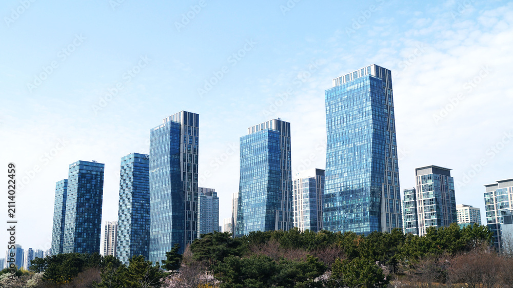 Fototapeta premium Modern glass office buildings in business district under a clear blue sky. Suitable for business, finance, architecture, urban development, real estate, smart city, and corporate presentation concepts