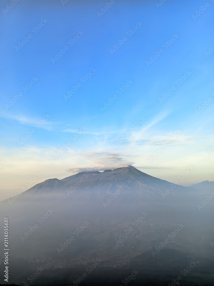 Fototapeta premium Volcano Peak at Sunrise with Sea of Clouds and Sun Rays in Blue Sky
