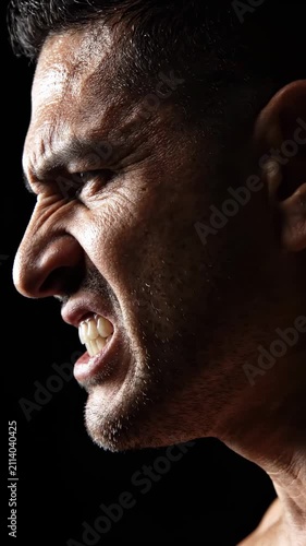 Close up profile of an angry man with gritted teeth showing intense emotion and aggression on a dark background