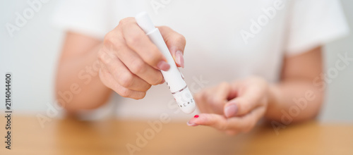 Foto Hand using lancet pen on finger with Blood drop glucose testing or Diabetes checking by digital blood glucose meter