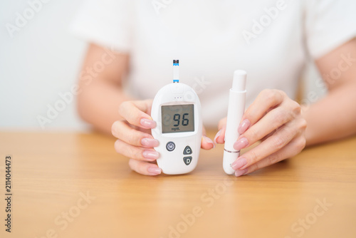 Foto Hand checking Diabetes or Blood glucose self testing by digital blood glucose meter with lancet pen