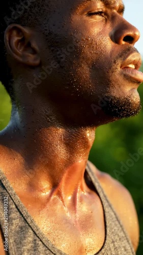Close-up of a determined Black man sweating profusely after an intense outdoor workout, his skin glistening under the sun, embodying peak physical effort and dedication