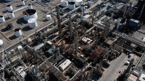 Aerial view of oil refinery featuring complex piping systems, tall distillation columns, and numerous storage tanks