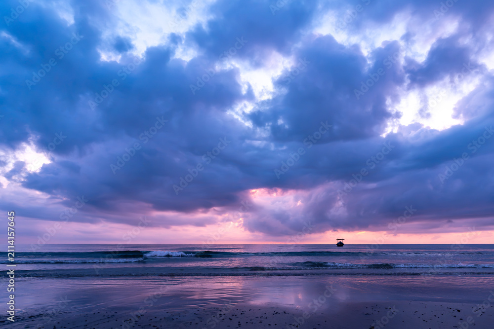 Obraz premium Dramatic Purple Ocean Sunrise with Silhouetted Boat and Moody Clouds