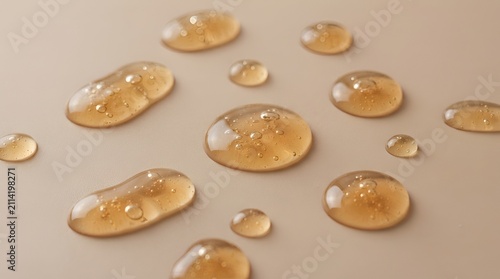 Transparent golden liquid drops on a smooth beige surface, showing viscous cosmetic serum or honey texture with small air bubbles inside