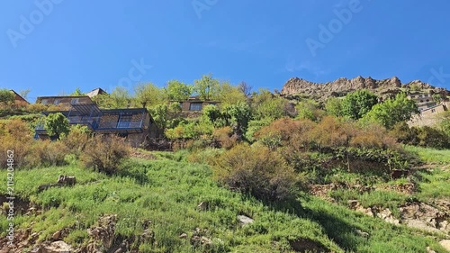 Rugged rocky outcrops crown a lush green hillside, where a traditional stone village nestles among trees beneath a vast blue sky with faint wisps of cloud.
📍 Hawraman Takht, Kurdistan, Iran 