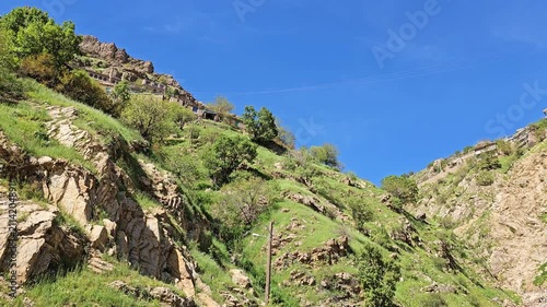Twin ridges of stone village houses rise sharply on either side of a steep rocky ravine, framed by green slopes under a bright blue sky with faint clouds.
📍 Hawraman Takht, Kurdistan, Iran 