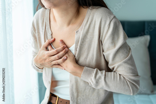 Young woman pressing her hands against her chest in pain, suffering from sudden chest pain or heart attack.